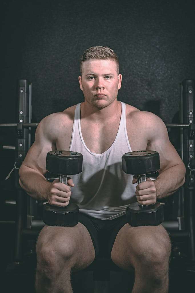 Concentrated bodybuilder with muscles working out with dumbbells in gymnasium