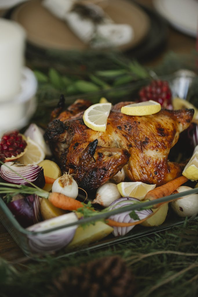 Roasted chicken with vegetables in glass roaster on table with fir sprigs
