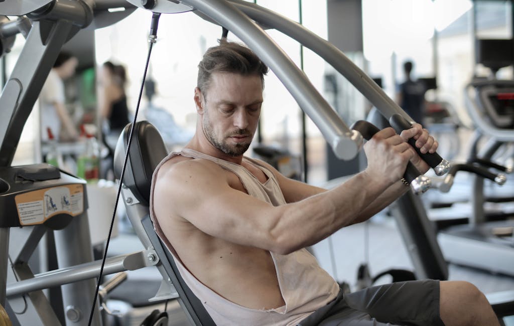 Side view of confident muscular man doing exercises on shoulder press machine while training in modern sports center