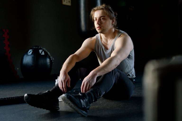 A male athlete rests after a workout session, sitting on the gym floor in calm reflection.