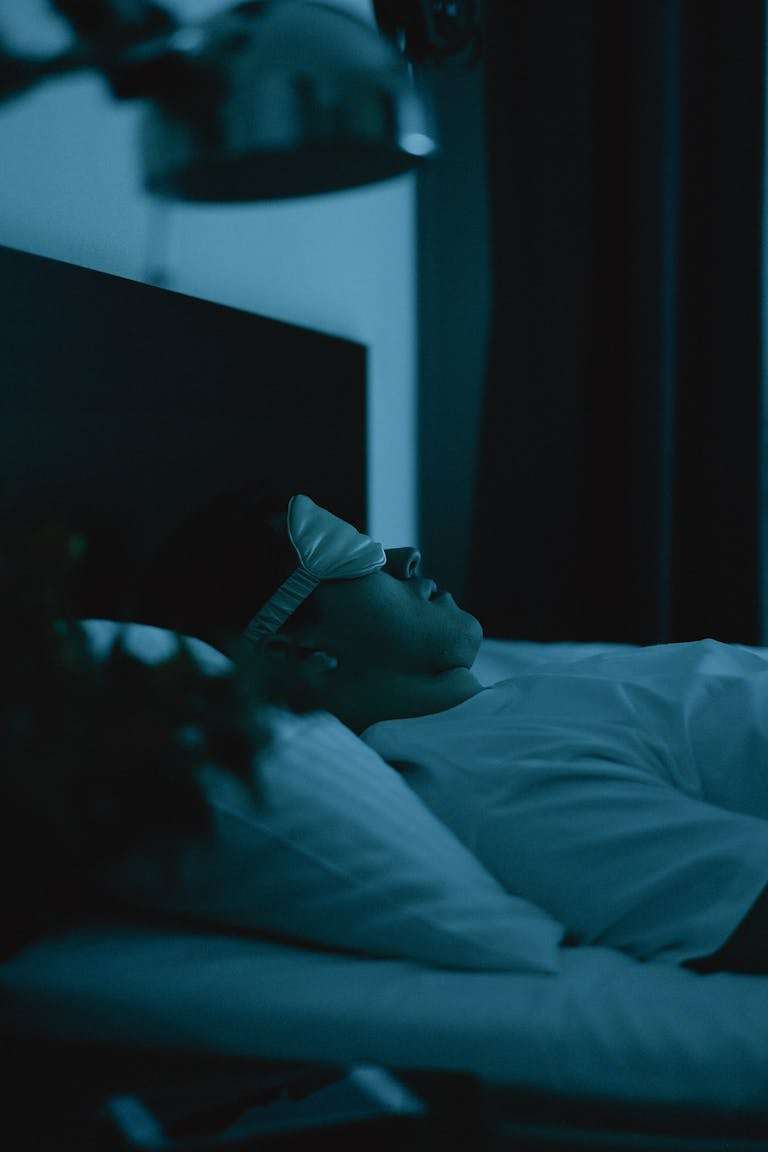 Adult resting peacefully in bed wearing a sleep mask, captured in a serene nighttime setting.