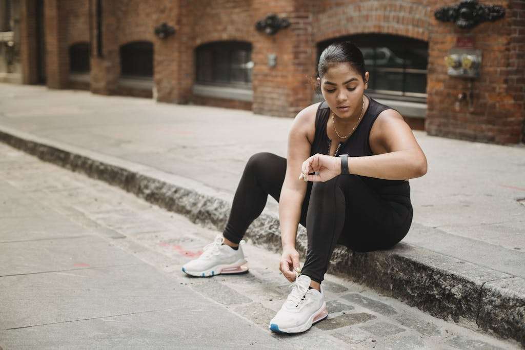 Woman in activewear checking smartwatch while sitting on urban sidewalk.